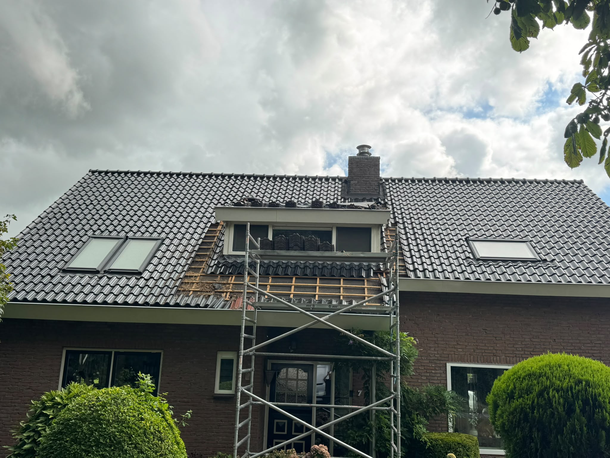 Dakkapel tijdens onderhoud, dakpannen deels verwijderd met steiger ervoor